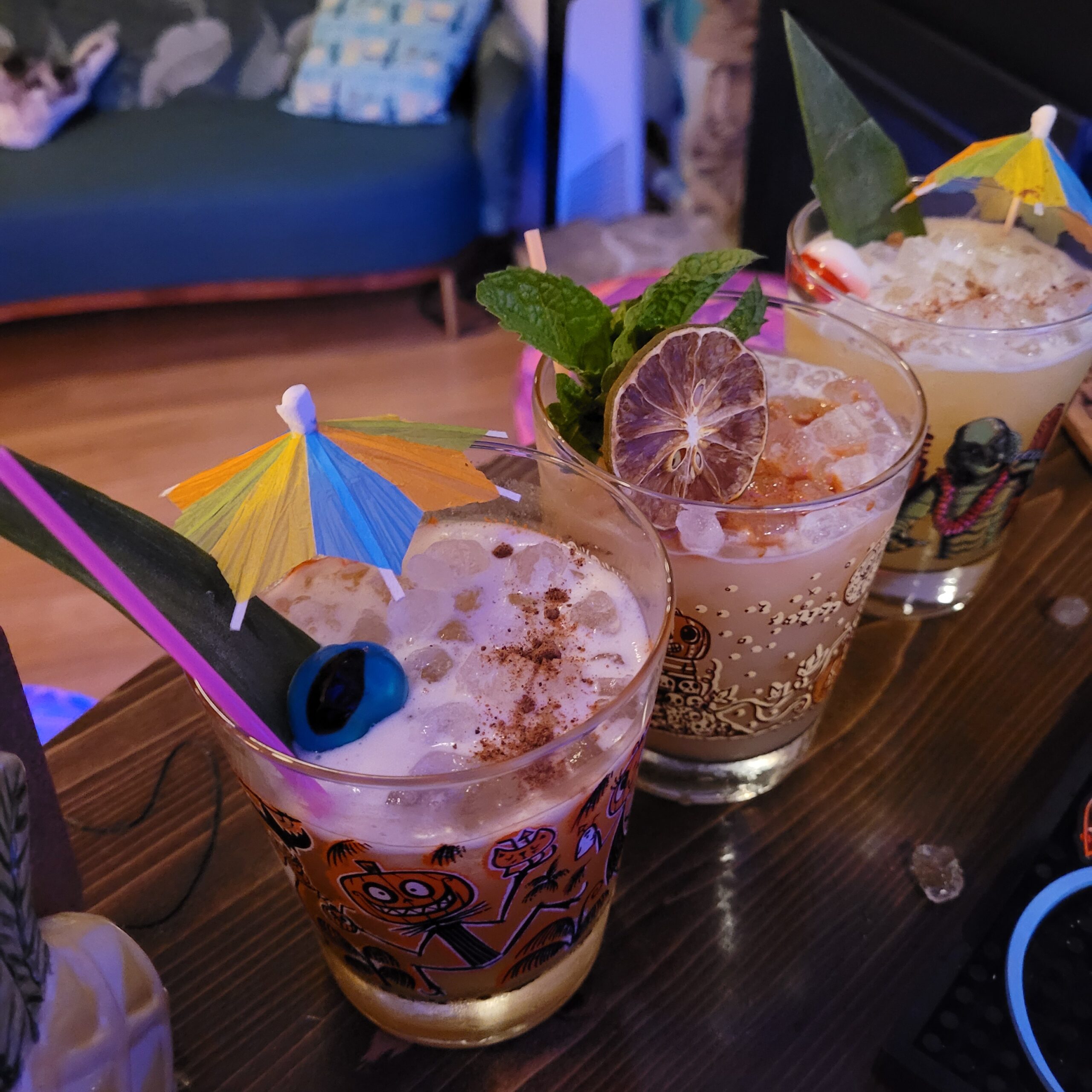 three mai tai cocktails with cute lime, mint, and pineapple frond garnishes lined up together in a home indoor setting at a slanted angle