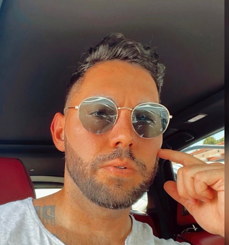 a young man poses for the camera in his car wearing sunglasses with an inquisitive look