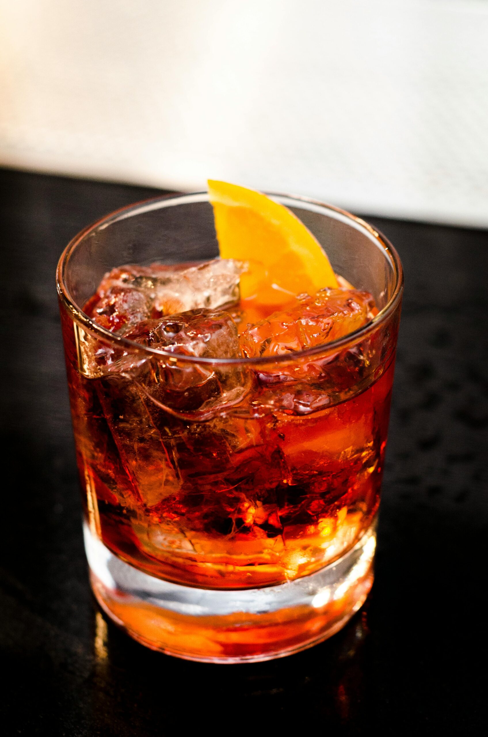 an old fashione cocktail with an orange wedge garnish is displayed on an indoor black countertop
