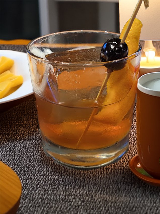 An Old Fashioned Cocktail on a table spread with foods spread out in a home setting