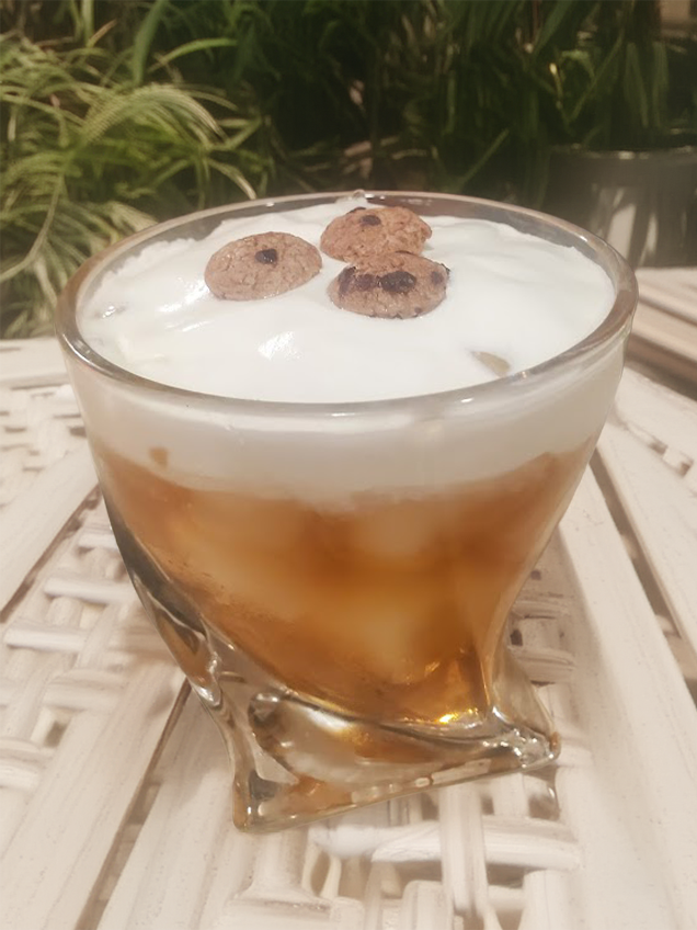 a white russian riff cocktail with cookie dough whiskey, whipped cream, and tiny cookie garnishes on a table outside