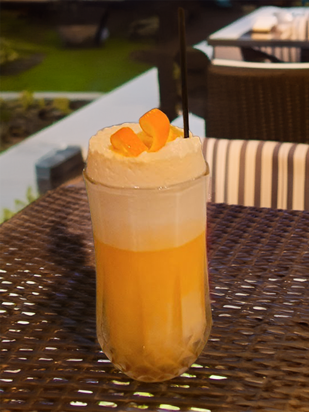 An Orange Creamsicle Cocktail on an outdoor patio table at night time.