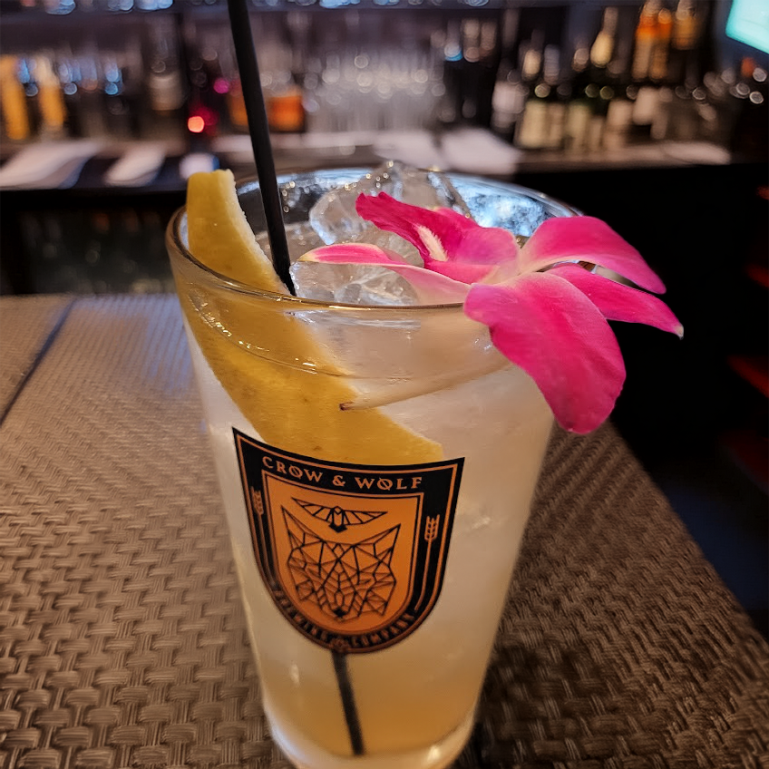 A Whiskey Highball with a lemon duke and orchid flower garnish at a nightclub bar setting